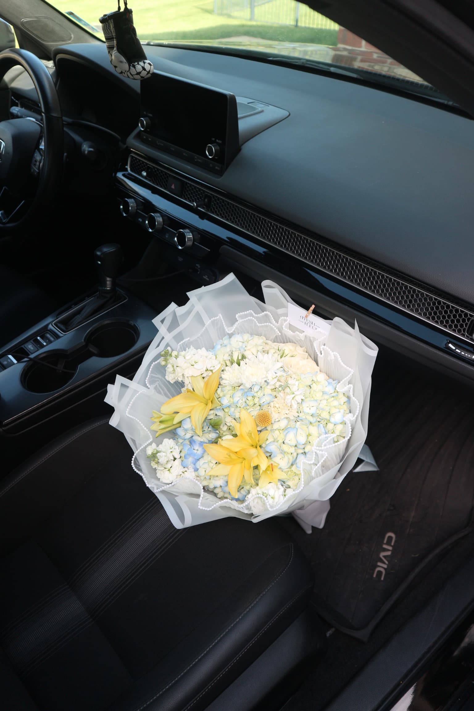 Bouquet of pale blue hydrangeas and yellow lilies in lace-edged white wrap on a car seat