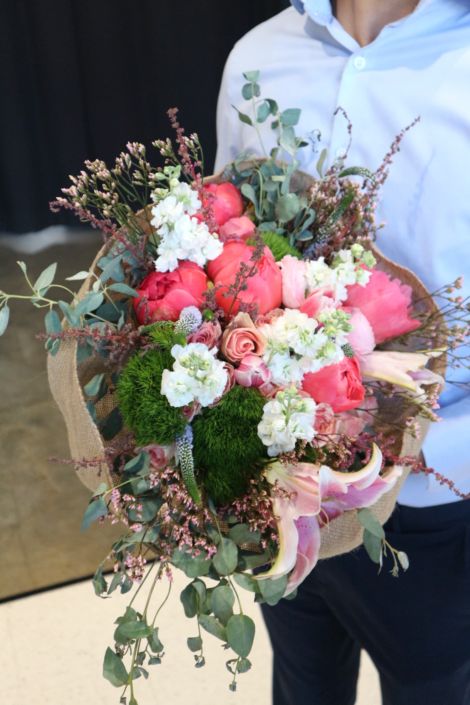 Coral peonies, pink roses and lilies with white stock, green dianthus and eucalyptus in burlap wrap