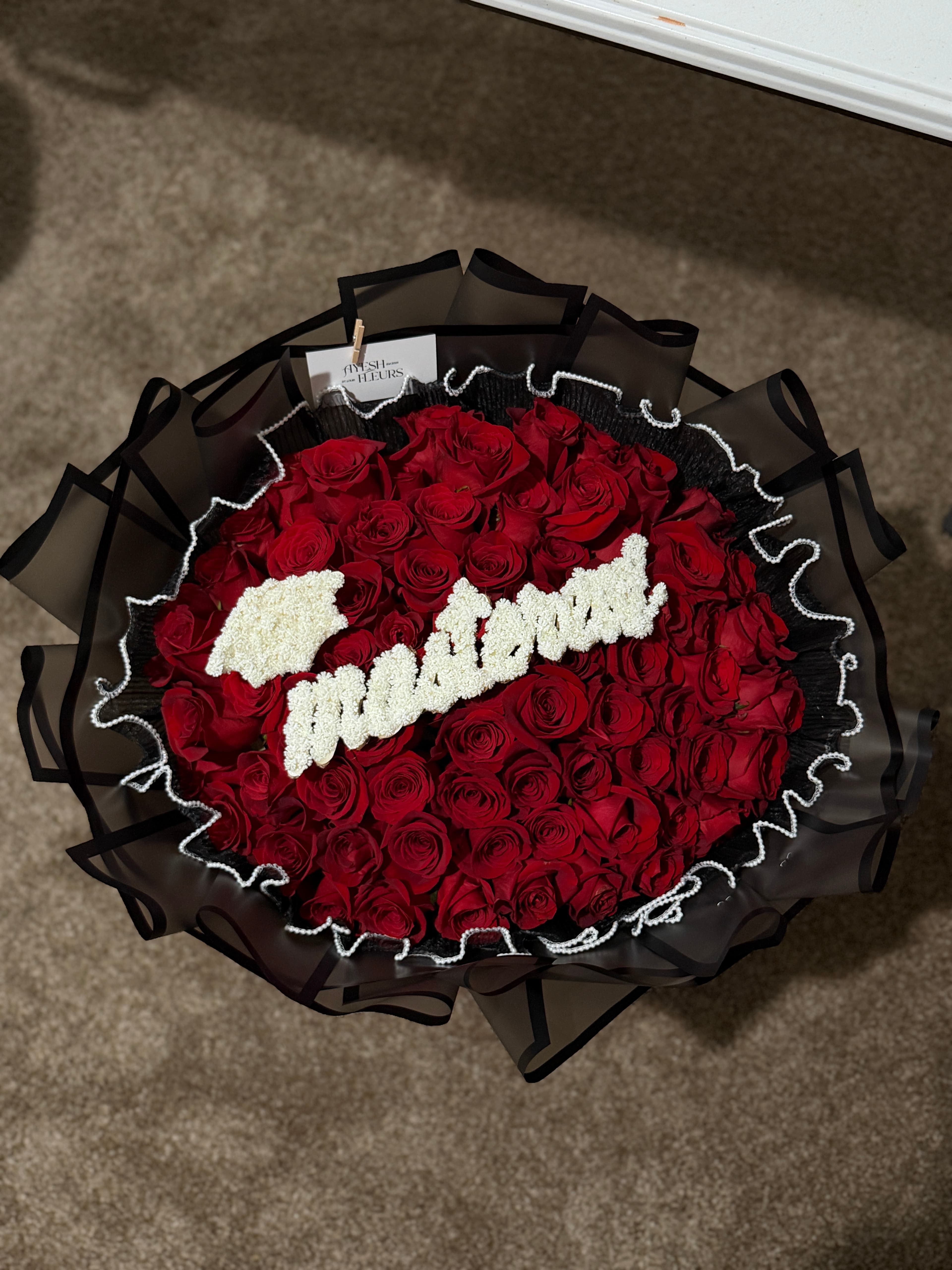Deep red roses with white script lettering, wrapped in black tulle edged with pearls