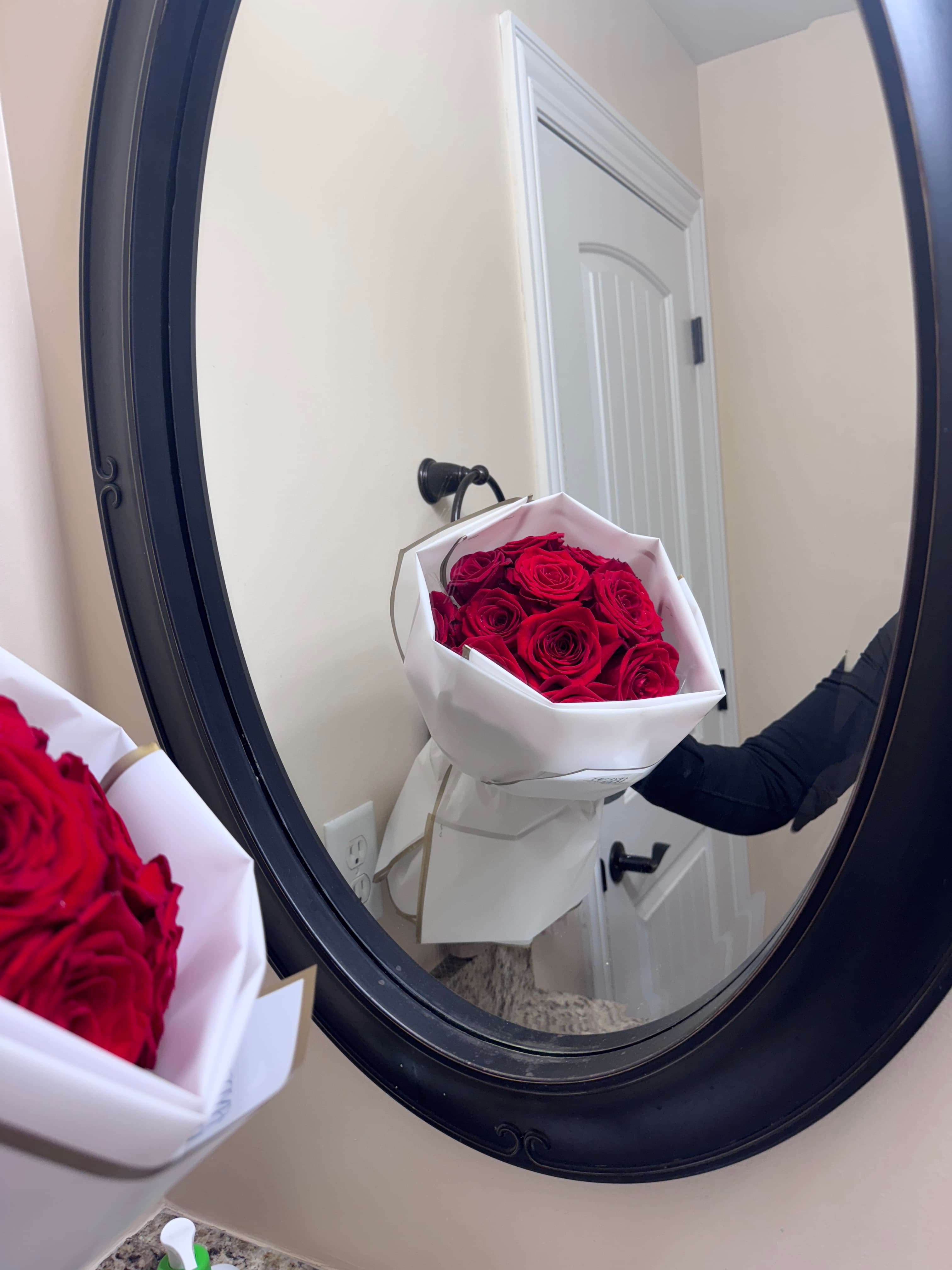 Red roses in a structured white wrap reflected in an oval black-framed mirror