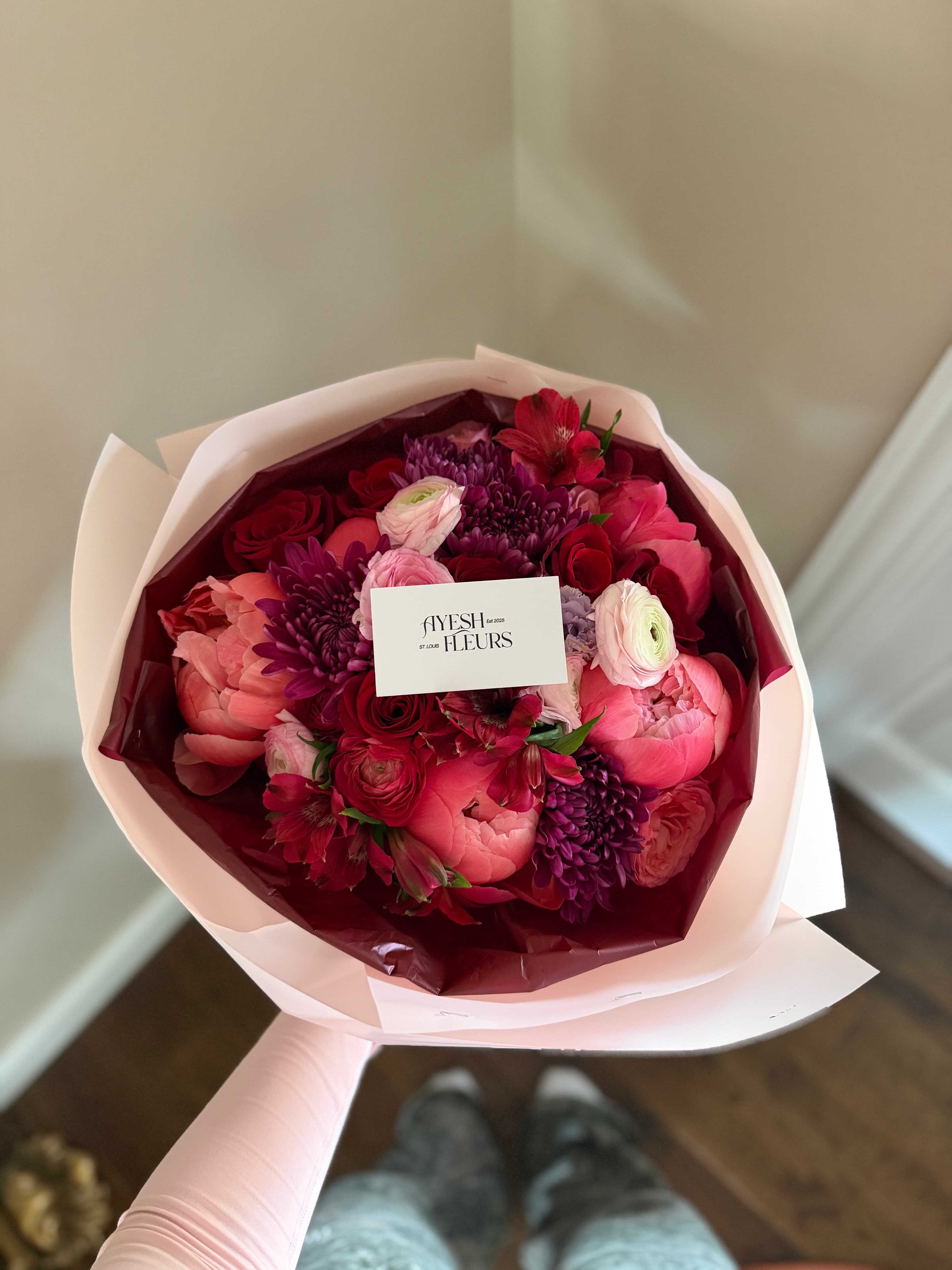 Coral peonies, red roses, purple mums and pink ranunculus in blush wrap with an Ayesh Fleurs card