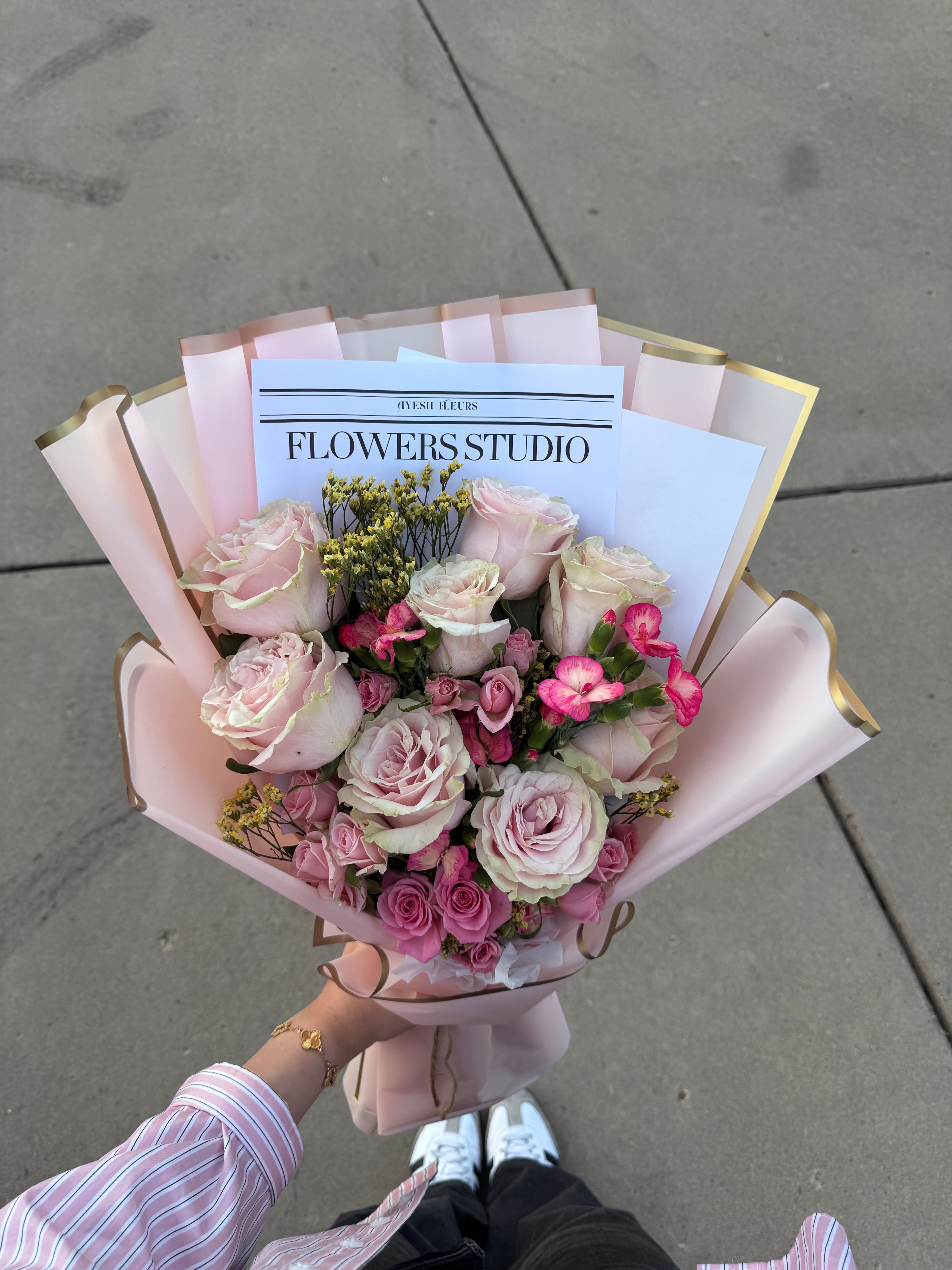 Blush and mauve roses with hot pink accents in gold-edged pink wrap, Flowers Studio card, held outdoors