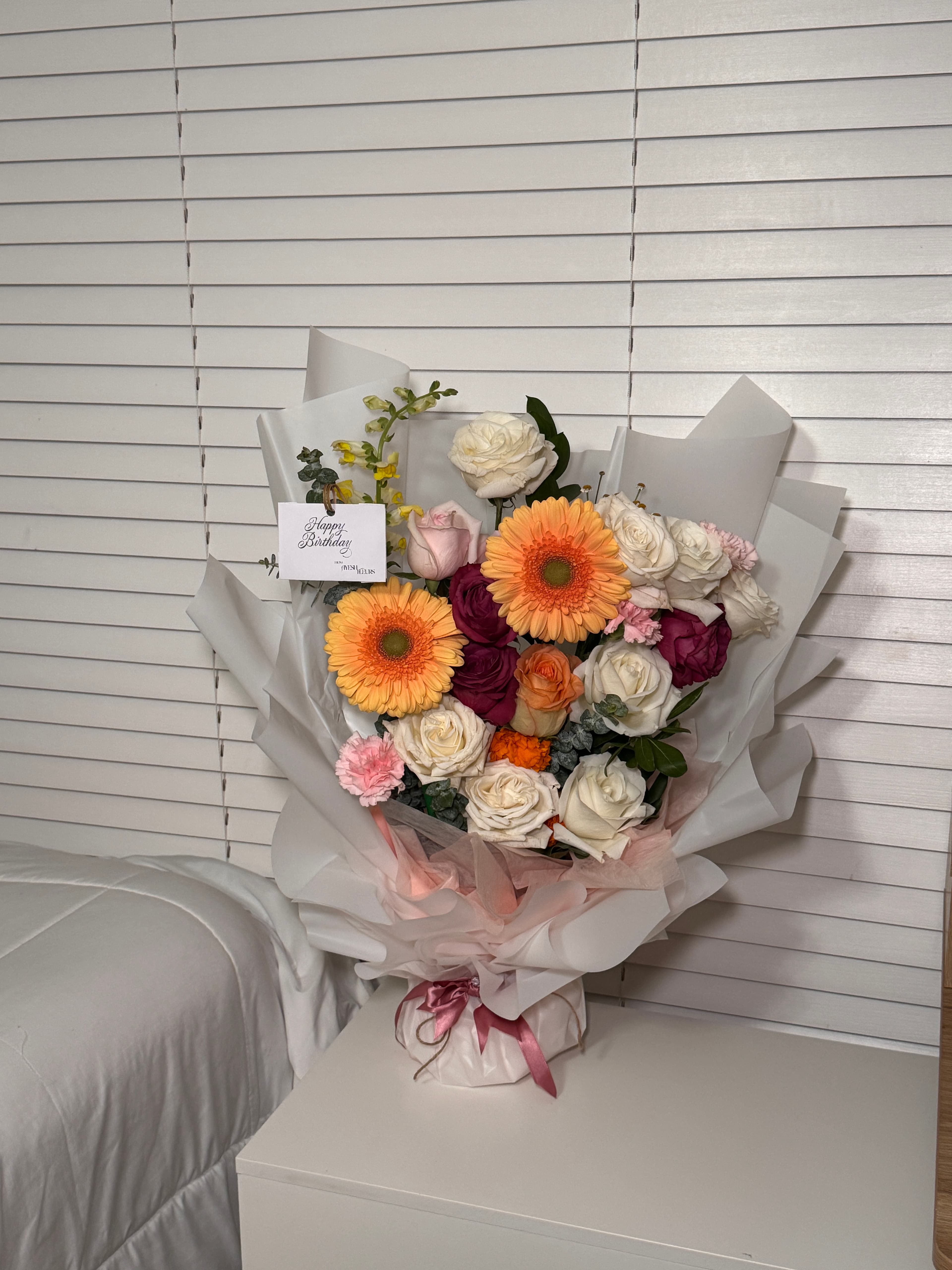 White and burgundy roses with orange gerbera daisies and a Happy Birthday card in a white wrapped bouquet