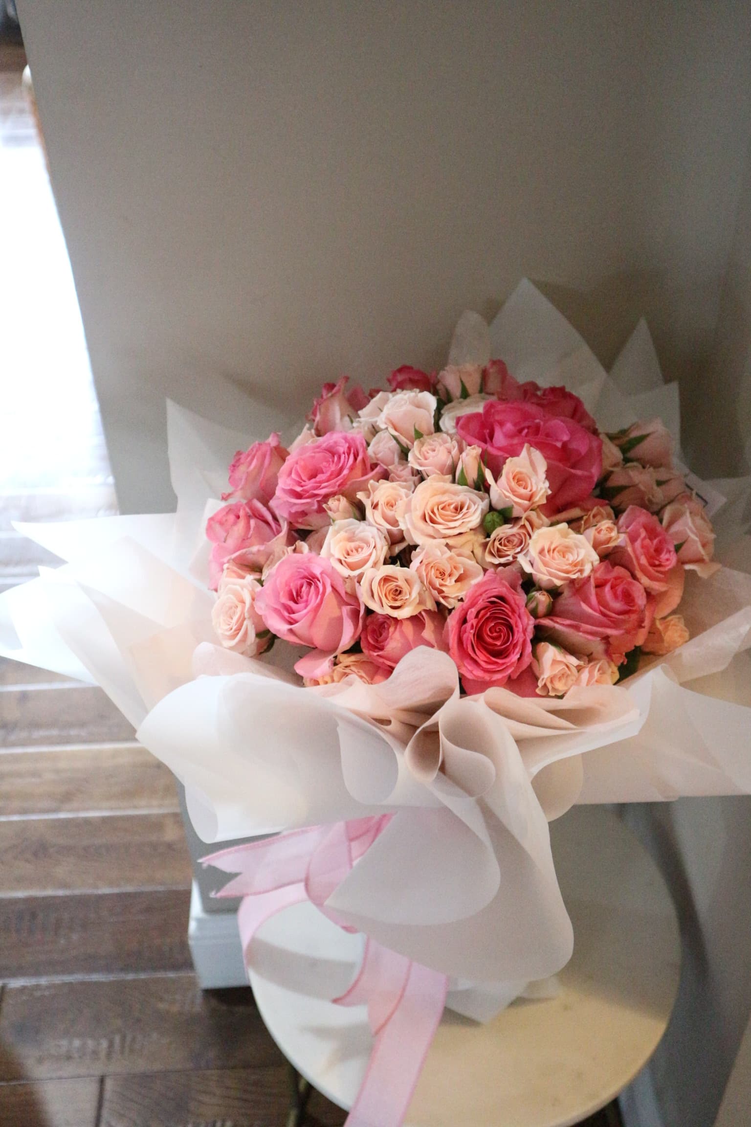 Pink and peach spray roses in white wrap, tied with a sheer pink ribbon
