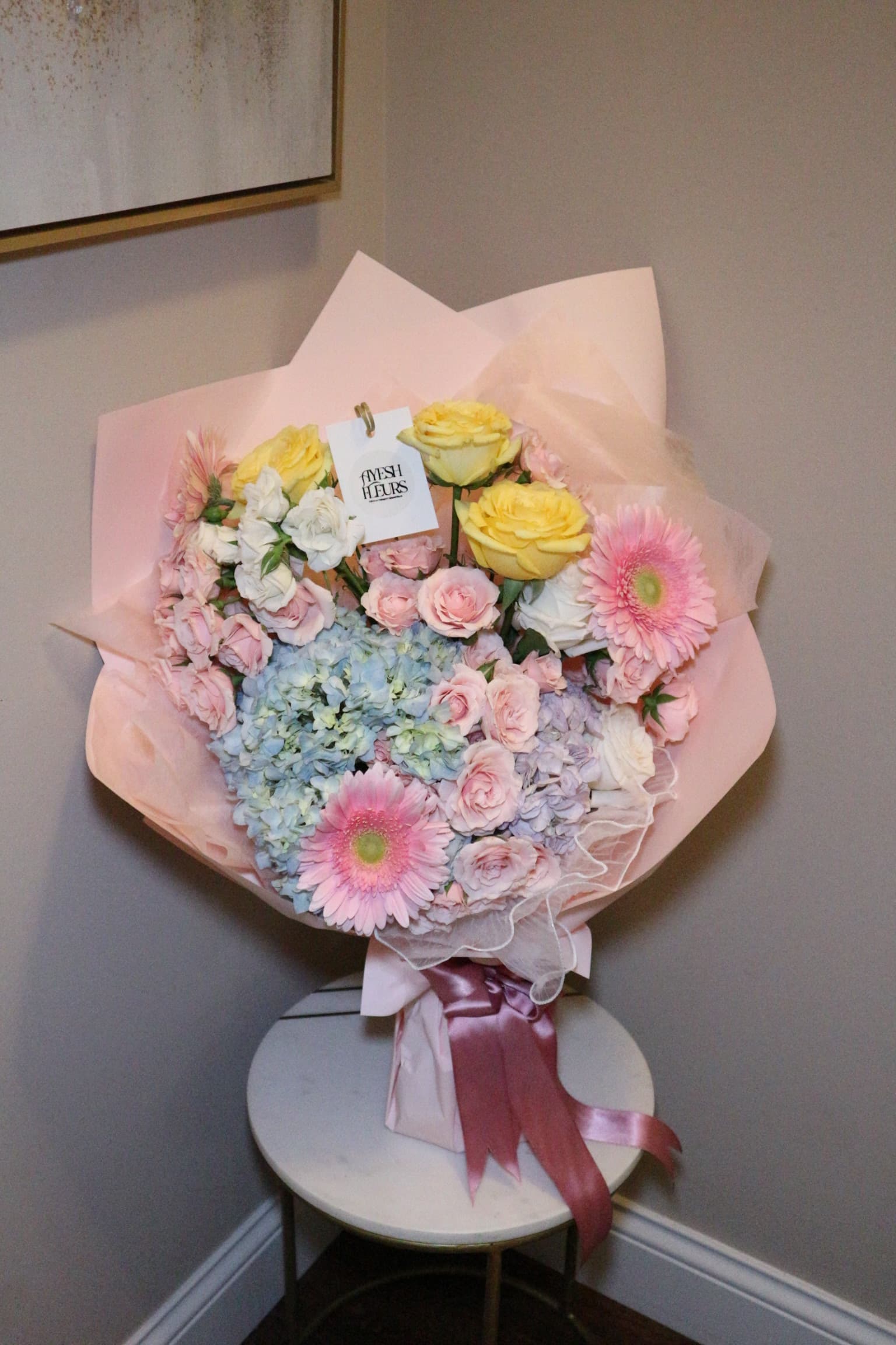 Pastel bouquet of blue hydrangea, pink gerberas, yellow roses and blush spray roses in pink wrap