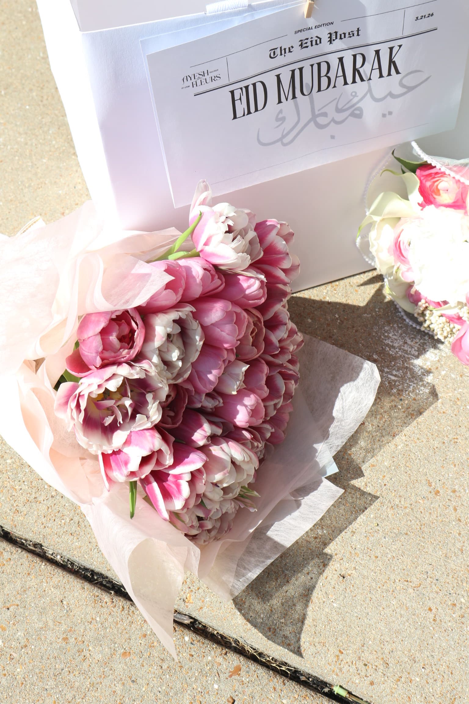 Pink double tulips in blush wrap beside a bouquet wrapped in The Eid Post Eid Mubarak newsprint