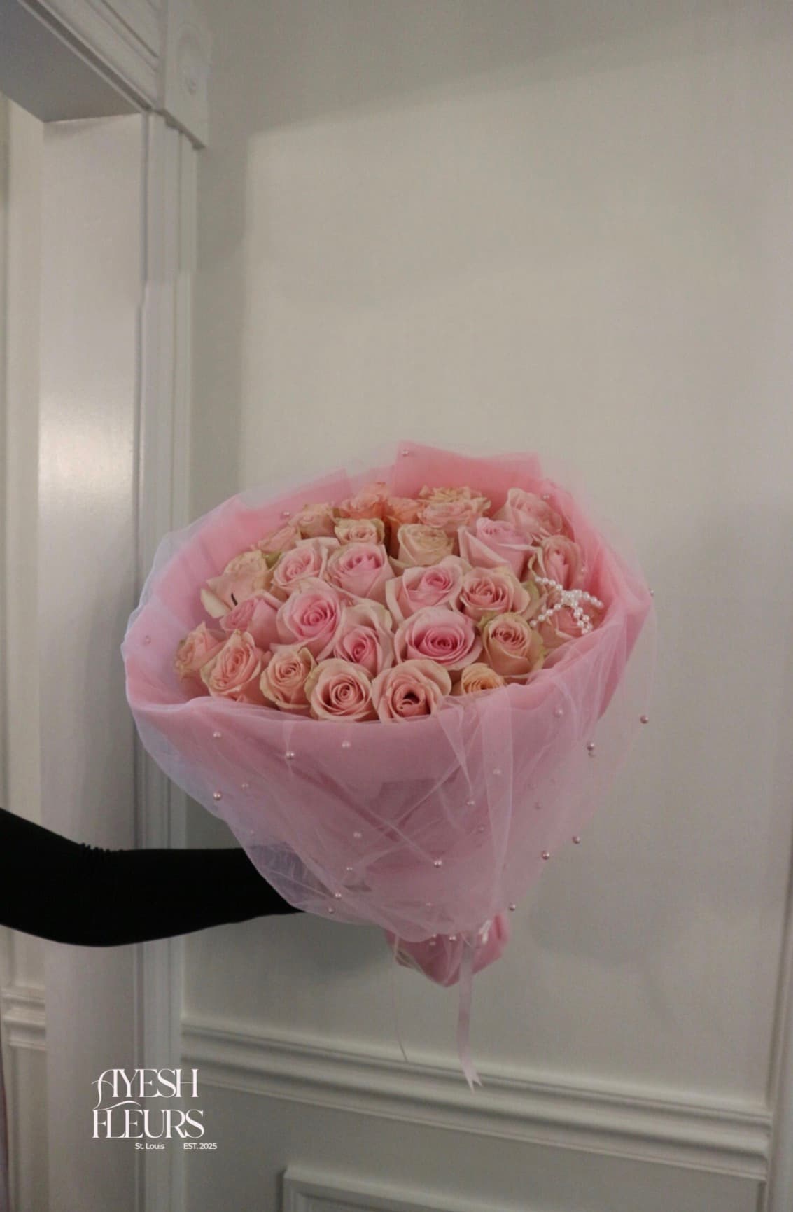Soft pink roses in pink tulle studded with pearls and a pearl bow, held on an outstretched arm
