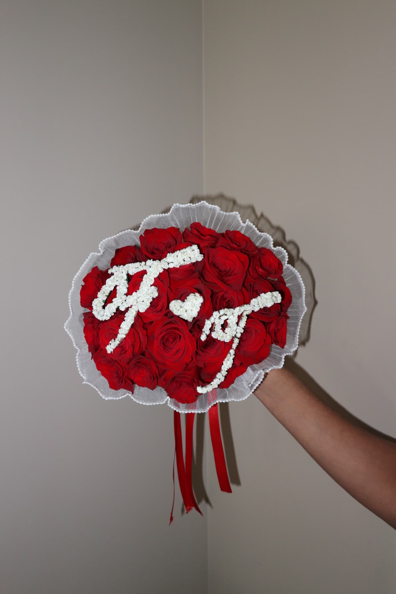 Red rose bouquet with Arabic lettering in white blossoms, tulle trim and red ribbons, held aloft