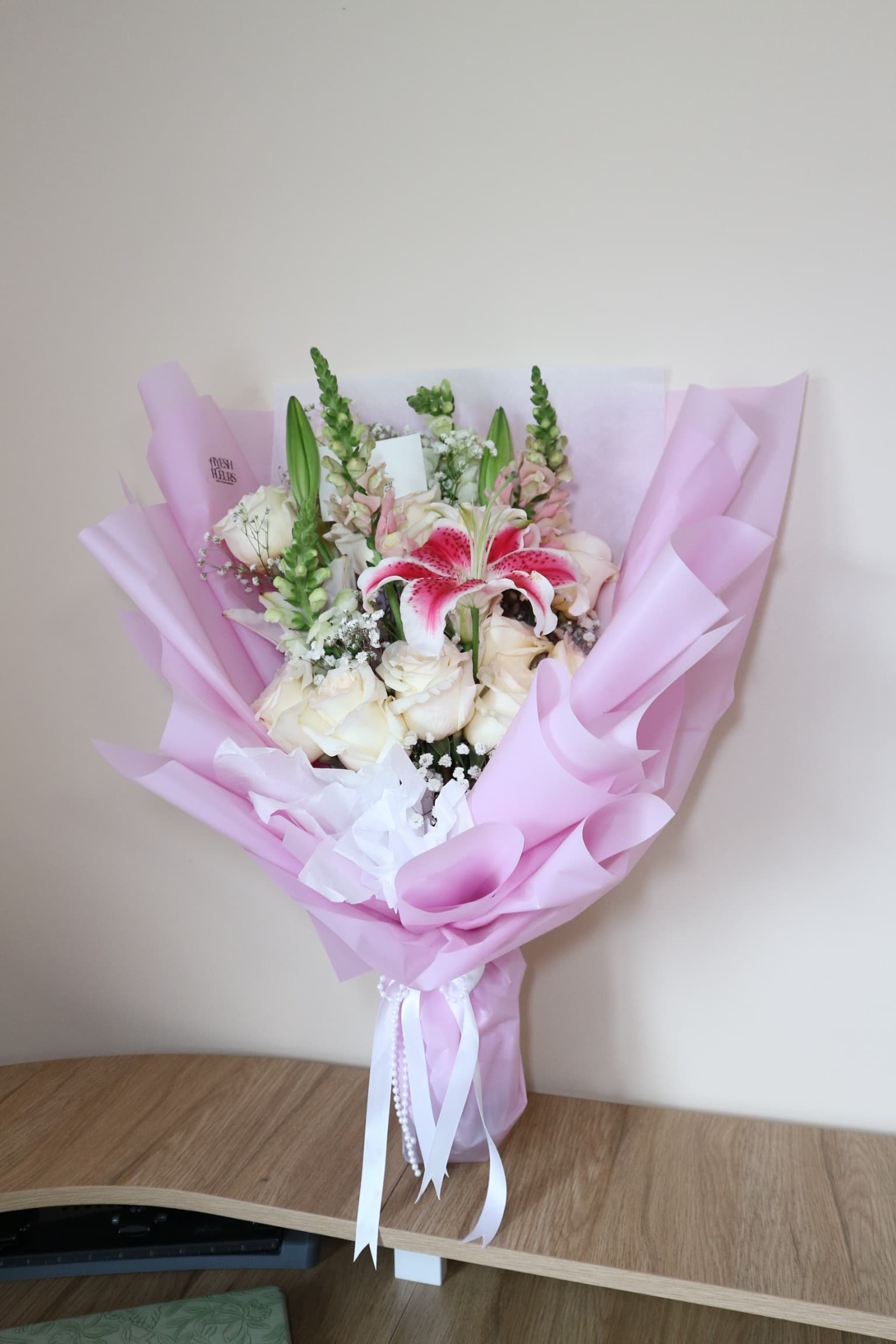 Cream roses, pink stargazer lily and snapdragons in pink wrap with pearl strands and ribbons