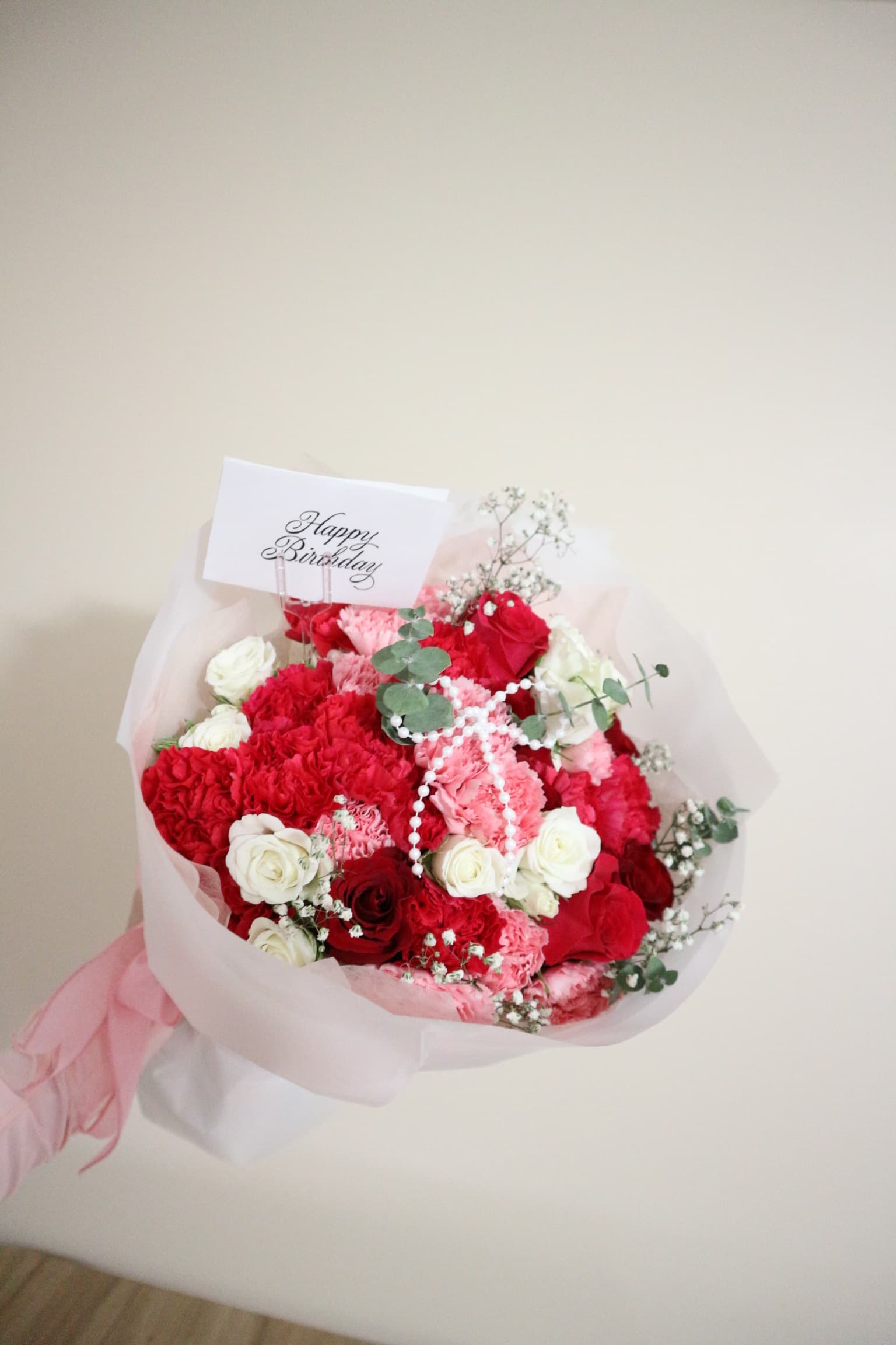 Red and pink carnations with white roses, pearls and a Happy Birthday card in sheer wrap