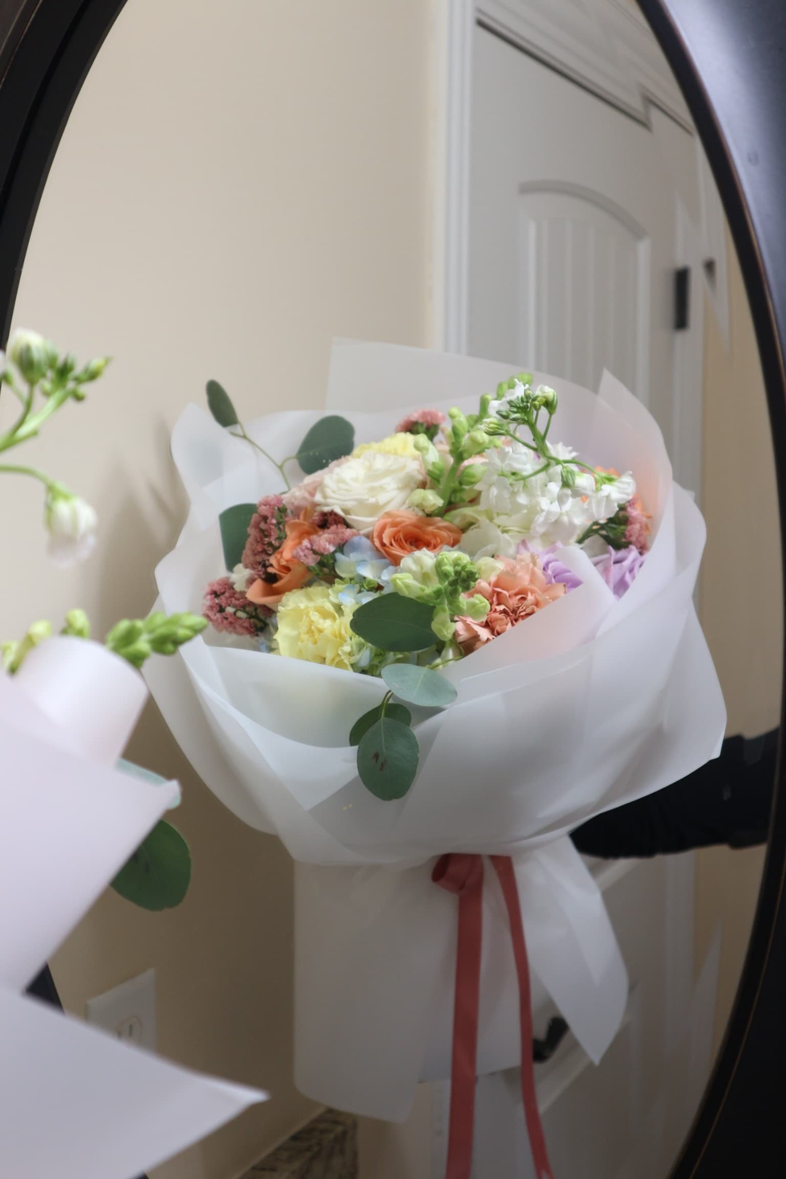 Pastel bouquet of peach roses, yellow carnation, stock and eucalyptus in white wrap with pink ribbon