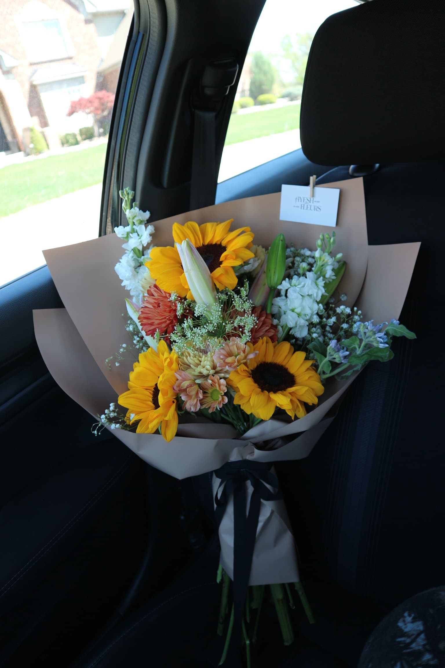 Sunflowers with orange daisies, white stock and baby's breath in tan wrap tied with black ribbon