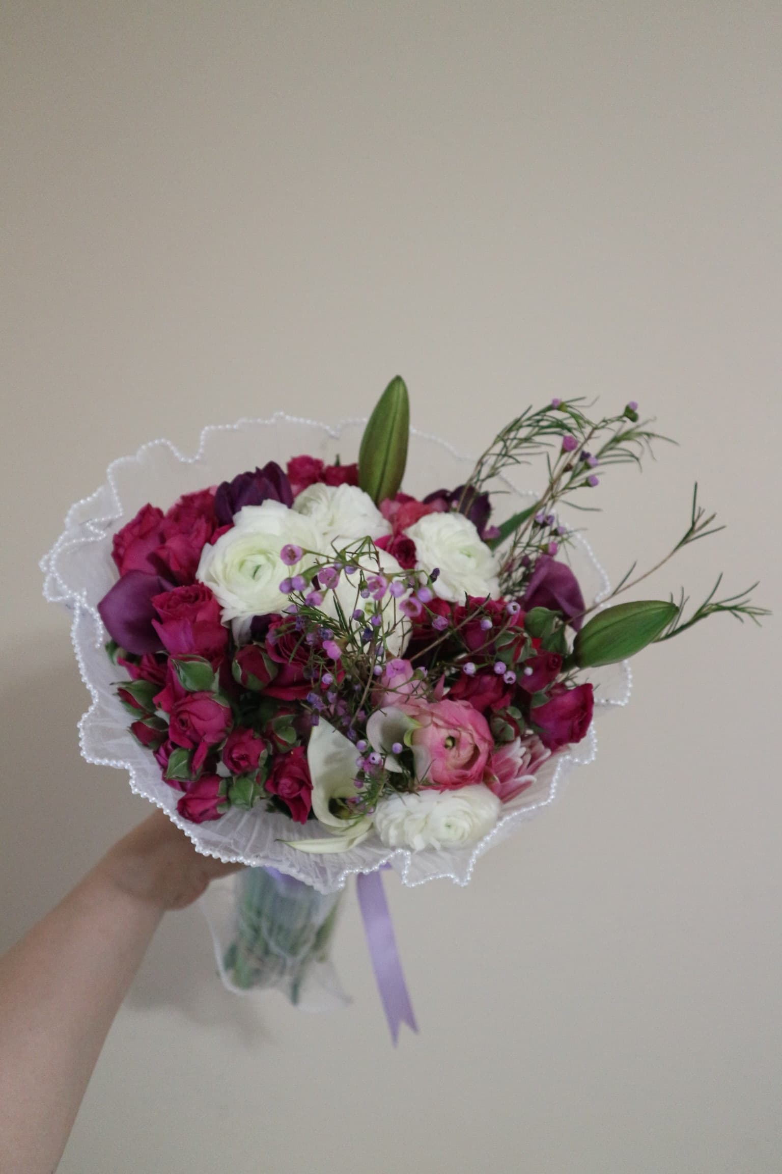 Magenta spray roses, white ranunculus, purple calla lilies and wax flower in pearl-trimmed white wrap